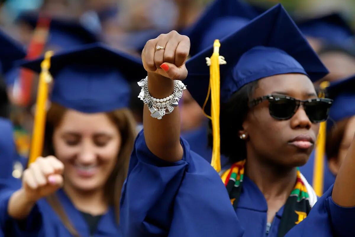 Black student raising her fist in cap and gown